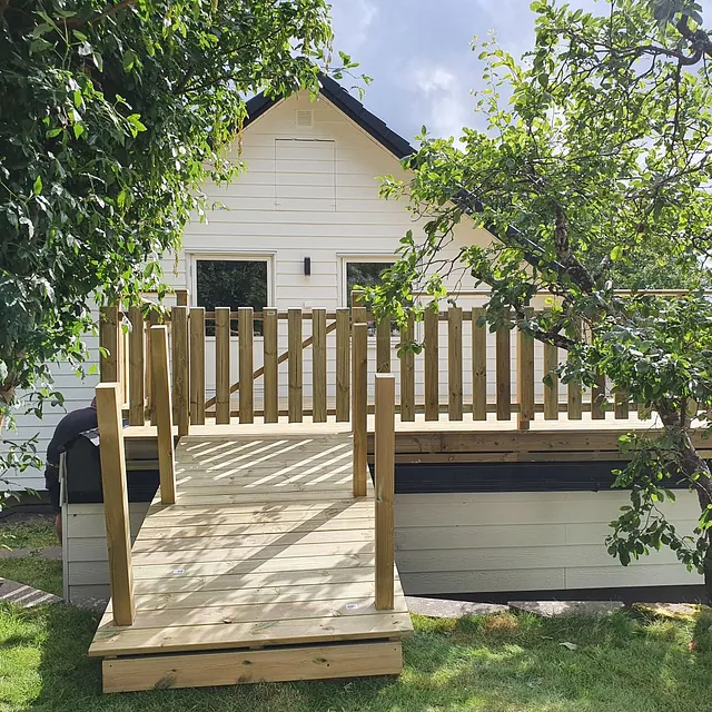 Nybyggd trätrappa och altan framför vitt hus.