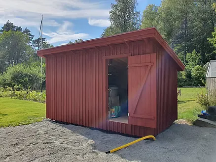Röd träbod med öppna dörrar på grusad gårdsplan.